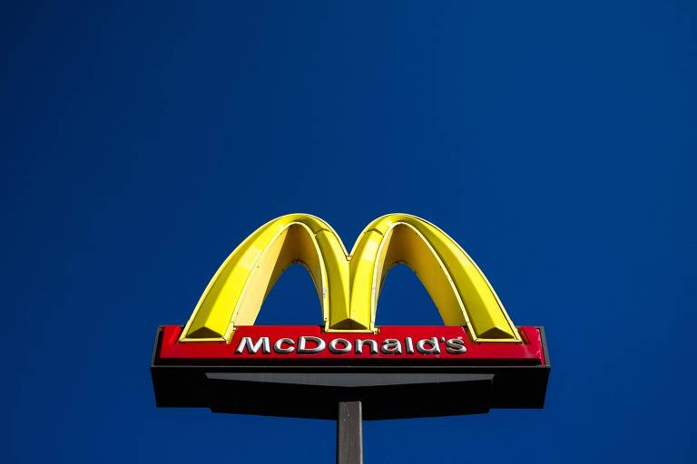 A imagem mostra o logotipo do McDonald039;s， que consiste em um grande 039;M039; amarelo em um fundo azul. Abaixo do 039;M039;， está escrito 039;McDonald039;s039; em letras brancas sobre uma faixa vermelha.
