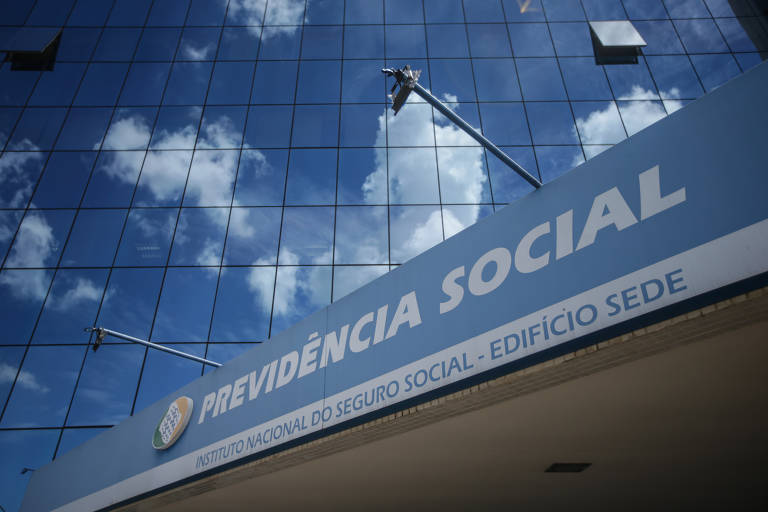 Foto de Gabriela Biló mostra a fachada da sede do INSS em Brasília. O p´redio tem vidros que espelham o céu azul e as nuvens brancas. Na frente da fachada lê-se: "Previdência Social - Instituto Nacional do Seguro Social - Edifício Sede"