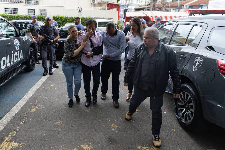 A imagem mostra uma cena de ação policial em uma área urbana. Várias viaturas da polícia estão estacionadas， e um grupo de pessoas está sendo acompanhado por policiais. Algumas pessoas parecem estar sendo detidas ou conduzidas， enquanto outras observam a situação. O ambiente é urbano， com prédios ao fundo e árvores nas proximidades.