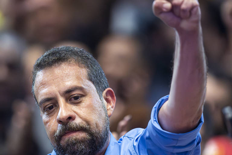 Fotografia mostra deputado federal e candidato Guilherme Boulos (PSOL) durante coletiva após a divulgação do resultado final das eleições em São Paulo. Ele é um homem branco, usa camisa azul e levanta o punho com um semblante cabisbaixo