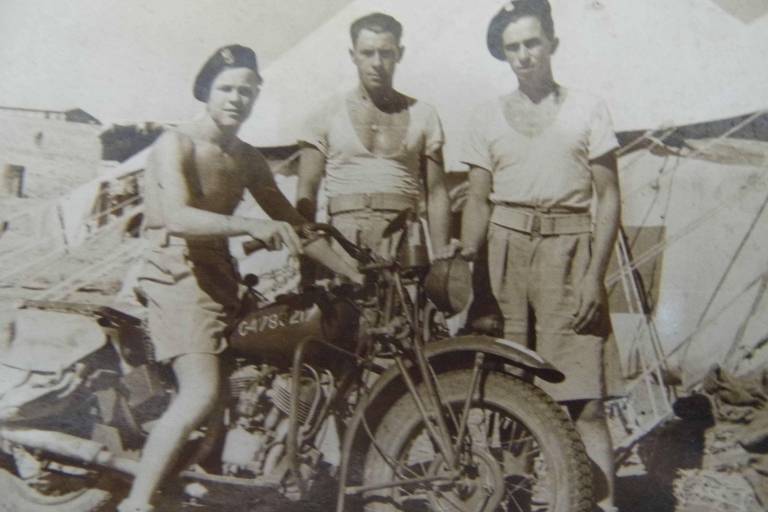 Andrzej Gasior, sem camisa, sentado em sua motocicleta ao lado de outros dois soldados