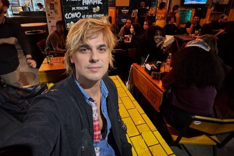 Em foto colorida, homem faz selfie na porta de uma bar