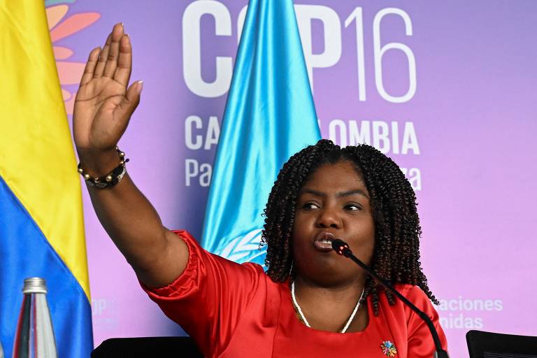 A vice-presidente colombiana Francia Márquez faz gestos enquanto fala durante uma coletiva de imprensa na Cop 16 em Cali, Colômbia. Ela tem cabelo crespo e trançado, veste uma blusa vermelha, levanta a mão direita, enquanto se expressa. Ao fundo, há bandeiras e um painel com o texto 'COP16 - Colômbia'.