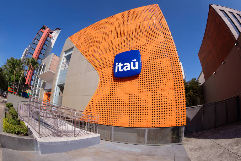 Fachada de agência do Itaú iluminada， com carros e ciclistas passando à frente