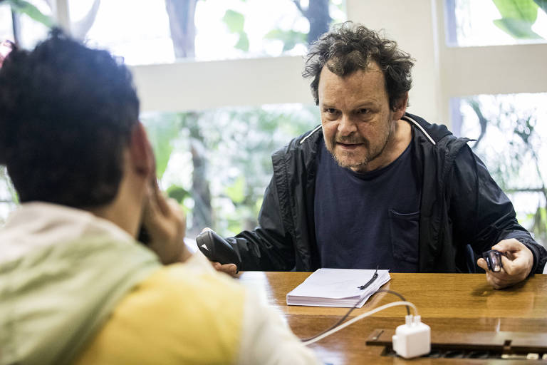 Em foto colorida, homem posa em frente a uma mesa 