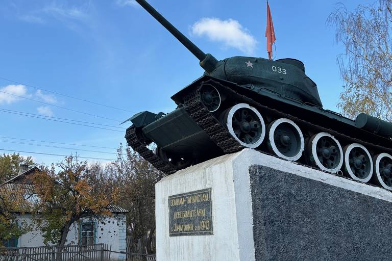 Monumento à Segunda Guerra com tanque T-34 em frente a casa destruída em Zatchatovki
