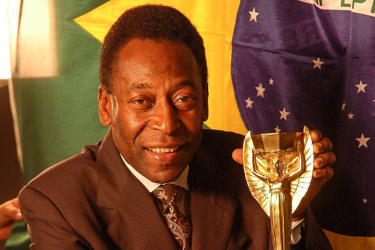 Pelé posa com troféu na mão em frente da bandeira do Brasil