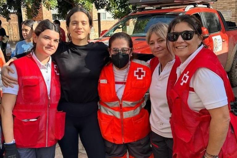 Em foto colorida, mulher de preto posa para foto com voluntários aos  moradores atingidos pela chuva em Valência, Espanha