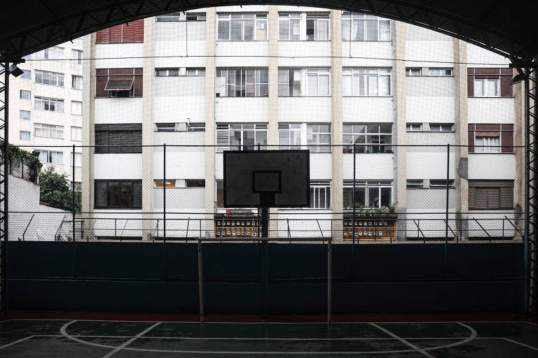 O muro e o telhado da quadra, mais escuros, formam uma moldura para a fachada cheia de janelas ao fundo