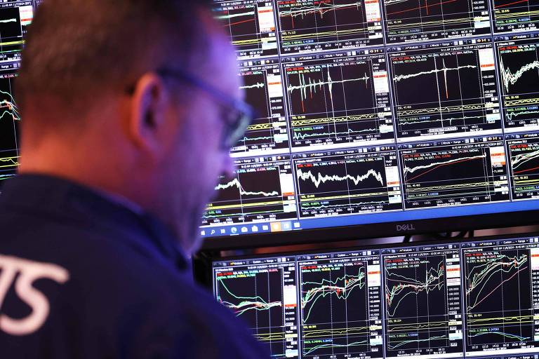 A imagem mostra um trader de costas， concentrado em múltiplos monitores que exibem gráficos financeiros e dados de mercado. Os gráficos têm linhas e indicadores， refletindo as flutuações do mercado. O ambiente parece ser uma sala de operações.