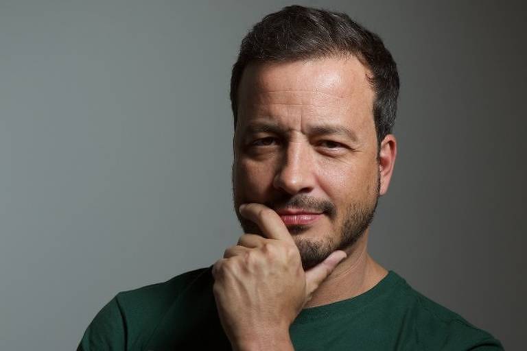 Em foto colorida, homem faz pose enquanto tira foto em um estúdio