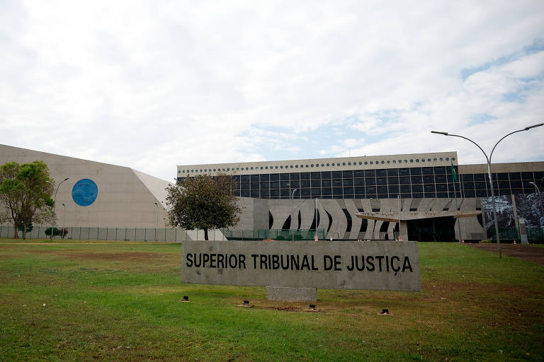 Imagem do Supremo Tribunal de Justiça, mostrando a fachada do edifício com um grande letreiro na frente. O céu está nublado e há algumas árvores e gramado na área externa.