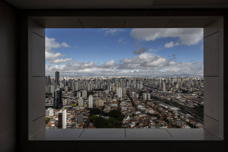 Emoldurada por uma janela, vista mostra centenas de prédis que parecem pequenos ao fundo