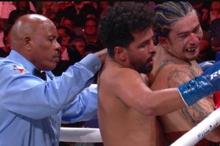 Em foto colorida, juiz de boxe separa dois lutadores em um canto do ringue de boxe