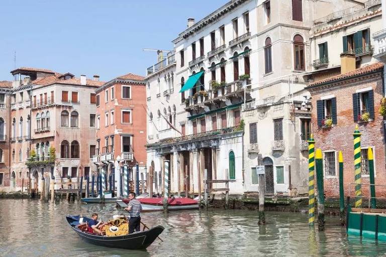 Em foto colorida, homens cruzam de barco a cidade de Veneza