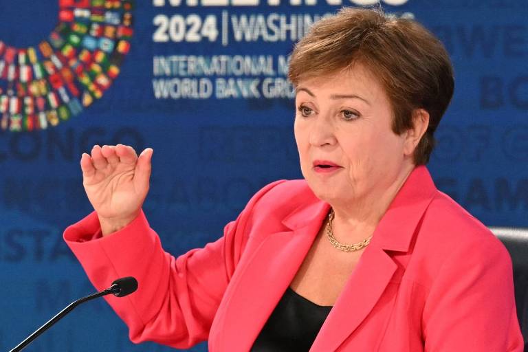 Usando um paletó cor de rosa e uma blusa preta， Kristalina Georgieva gesticula com a mão direita ao falar a um microfone posicionado em sua frente