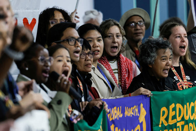 Um grupo diversificado de pessoas está participando de uma manifestação, segurando cartazes e gritando em apoio a uma causa. As expressões faciais mostram determinação e paixão. Algumas pessoas estão usando óculos e há uma variedade de estilos de cabelo. O fundo é desfocado, mas sugere um ambiente de evento ou conferência.