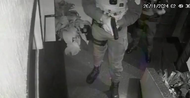 O estudante continua no chão e o policial mantém a arma em punho apontada em sua direção