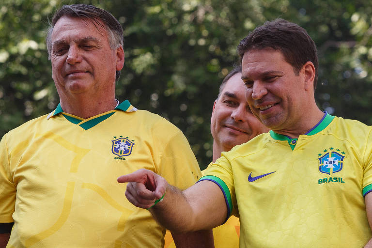 Dois homens brancos, com camisa da seleção brasileira, da região da cintura para cima. Eles estão lado a lado