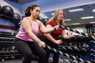 A personal trainer helps a client properly grip battle ropes at a gym in Elkridge, Md., Nov. 10, 2022. (Dave Cooper/The New York Times)