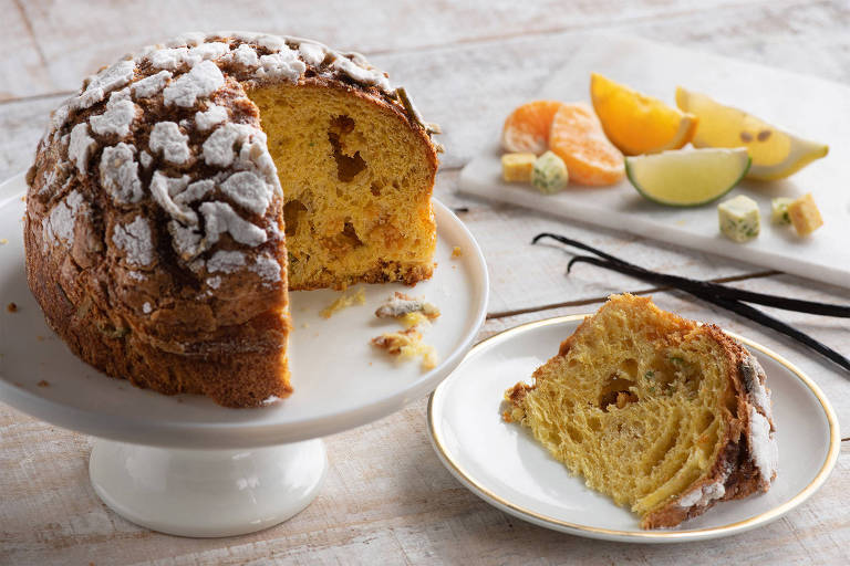 A foto mostra um panetone fatiado com cobertura de creme de amêndoas. Ao fundo， um prato com fatias de frutas cítricas como limões e tangerinas