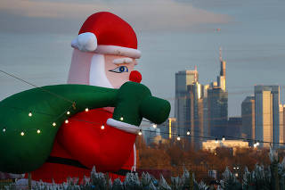 A huge inflatable Santa Claus figure advertises a Christmas tree shop in front of the skyline in Frankfurt
