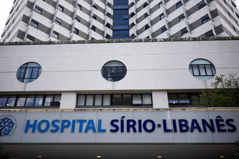 Fotografia mostra a fachada do hospital Sírio-Libanês em São Paulo. É possível ver parte do prédio e as janelas, assim como uma grande placa escrito: "Hospital Sírio Libanês"