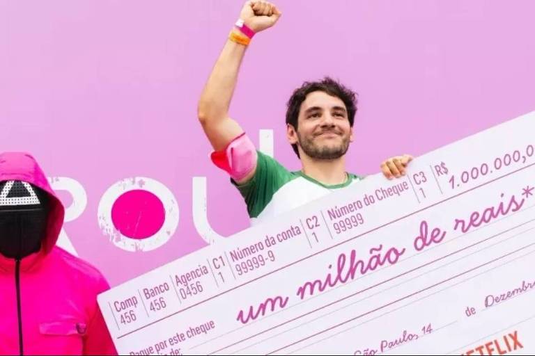 Em foto colorida, homem exibe o cheque de R$ 1 milhão ao vencer desafio de série coreana da Netflix