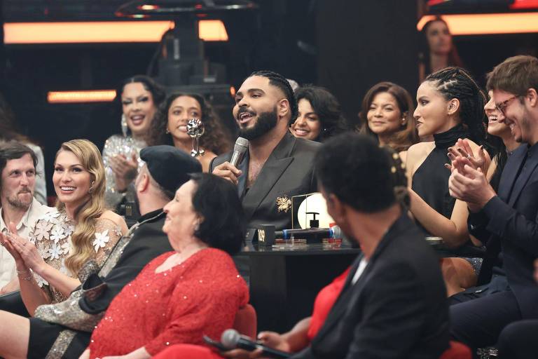 Em foto colorida, homem de terno preto brinca no palco no programa de auditóriori