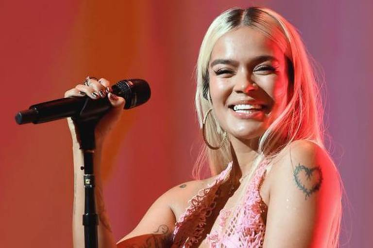 A cantora colombiana Karol G segura um microfone e sorri enquanto se apresenta em um show em Los Angeles