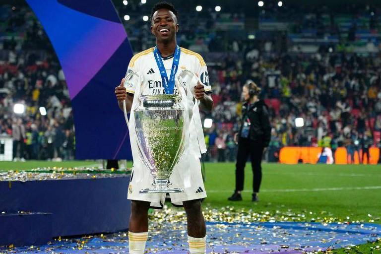 Vinícius Júnior segurando troféu de campeão da Liga dos Campeões da UEFA enquanto sorri