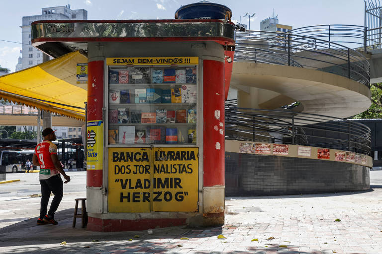 Banca de revista nas cores vermelha e amarela. Na lateral da banca,  está escrito 'Banca e livraria dos jornalistas Vladimir Herzog'