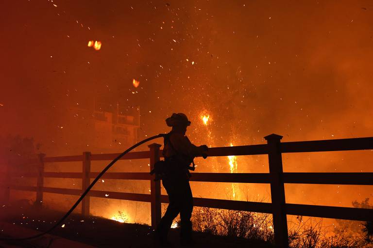 Um bombeiro tenta combater o incêndio florestal perto de um prédio em Malibu, na Califórnia (EUA)