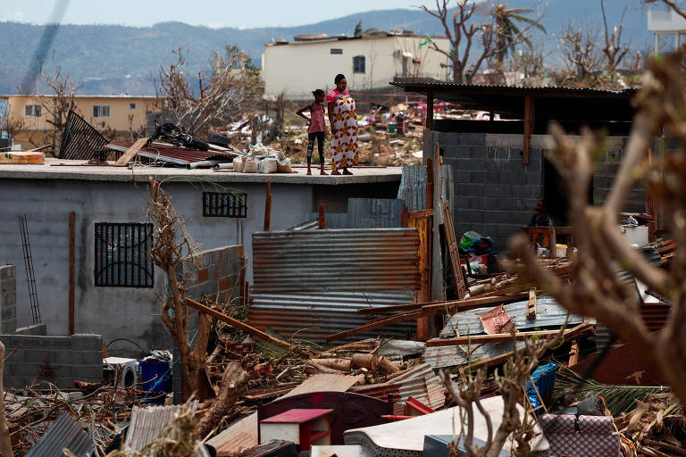 Mulheresno telhado enquanto observam casas destruídas após passagem do ciclone Chido, em Mayotte