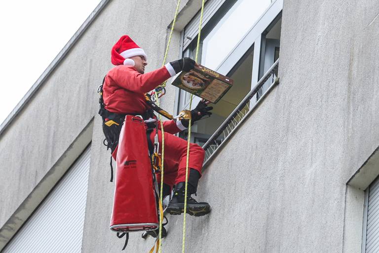 Homem vestido de Papai Noel desce de rapel do telhado de um hospital para entregar presentes para crianças em Zagreb, na Croácia