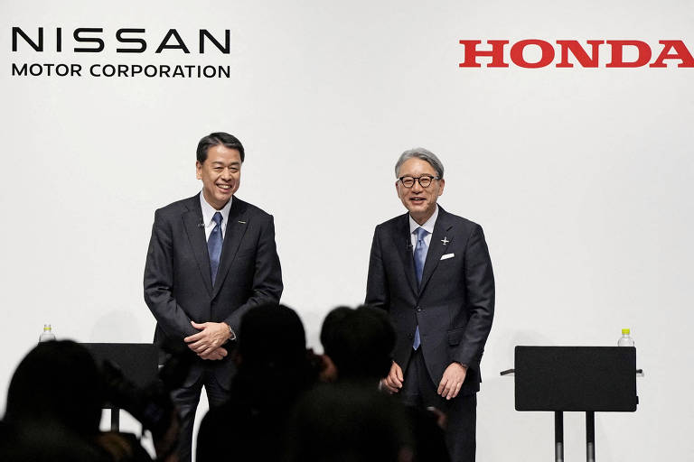 A imagem mostra dois homens em trajes formais, sorrindo e posando em um evento. À esquerda, há um logotipo da Nissan Motor Corporation e, à direita, um logotipo da Honda. O fundo é claro e há uma plateia visível em silhueta.