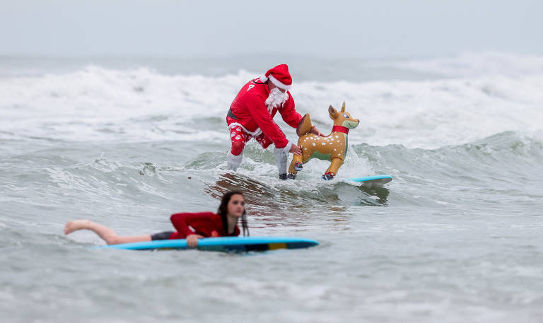 Surfista vestido de Papai Noel coloca rena de plástico na frente de sua prancha no evento anual Surfing Santas Christmas Eve em Cocoa Beach, na Flórida (EUA)