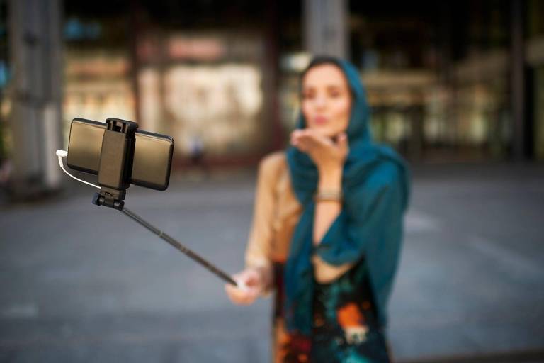 Mulher gravando um vídeo com um pau de selfie， desfocado no fundo
