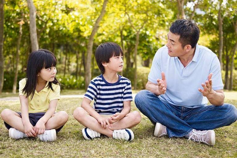 Um homem conversando com duas crianças em um parque
