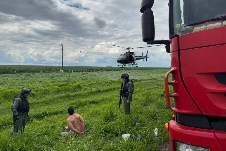 homem ajoelhado no mato， rendido por policiais 