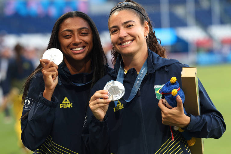 Sorrindo e exibindo suas medalhas， Kerolin e Angelina festejam a conquista da prata nas Olimpíadas de Paris pela seleção brasileira feminina de futebol