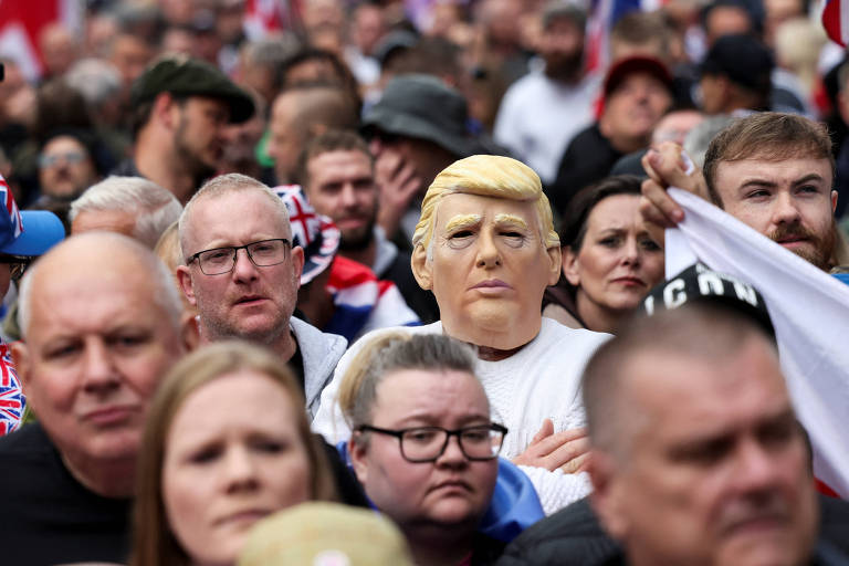 Manifestantes brancos de meia idade. no meio, vê se alguém com máscara do rosto de donald trump (branco e loiro de meia idade)