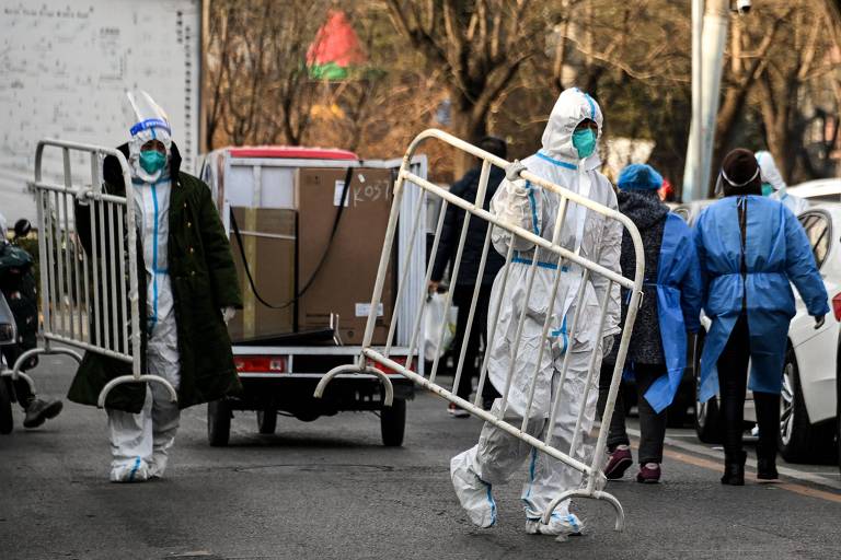 Trabalhadores de saúde usando equipamentos de proteção individual (EPI) carregam barricadas dentro de uma comunidade residencial após um bloqueio devido às restrições do coronavírus Covid-19， em Pequim， na China