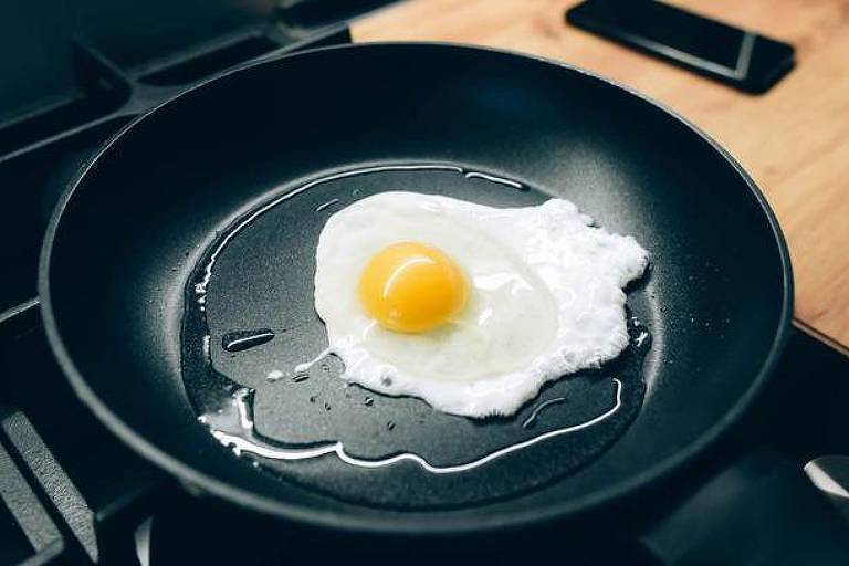 Foto mostra uma frigideira preta fritando um ovo. 