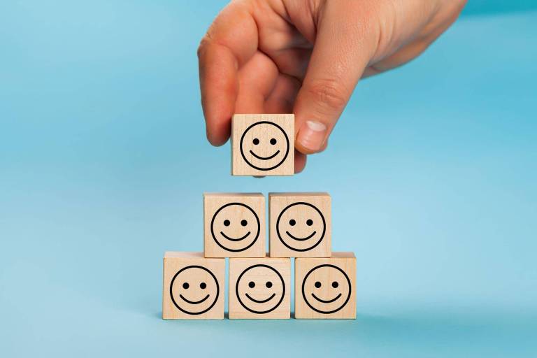 Mão colocando cubo com carinha feliz impressa em cima de pilha com cubos iguais
