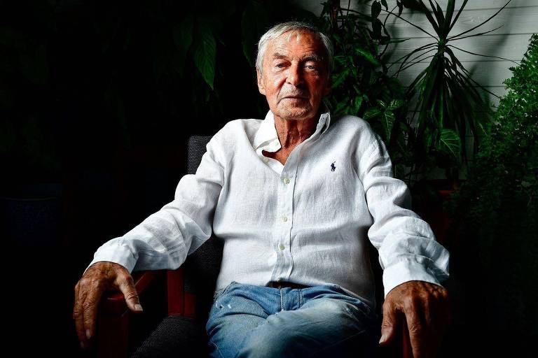 Erno Rubik posando para foto， sentado em cadeira， com sorriso tímido
