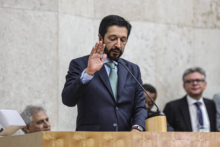 A imagem mostra Ricardo Nunes em pé na frente de um púlpito com a mão direita levantada durante juramento 