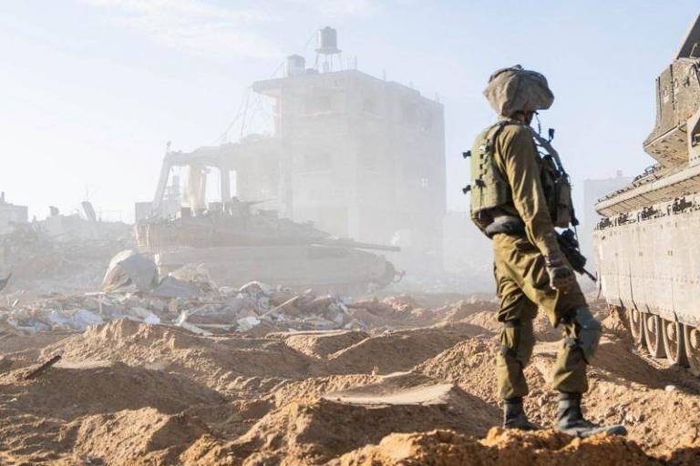 Foto mostra soldado de costas olhando para uma casa destruída.