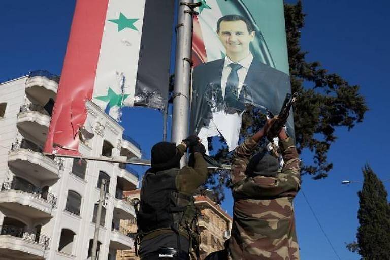 Foto mostra dois homens com roupa militar camuflada tirando cartaz de Assad em poste