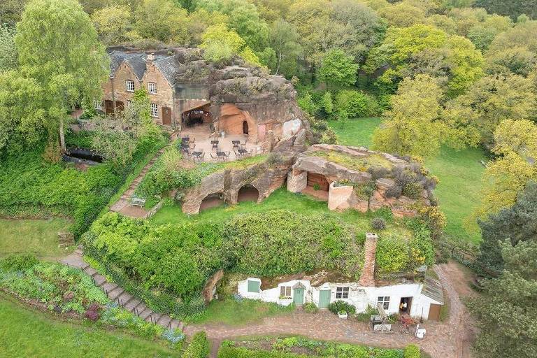 Uma imagem aérea de drone mostrando casas construídas na encosta de uma colina com portas e janelas cortadas no arenito. Algumas aberturas de cavernas podem ser vistas.
